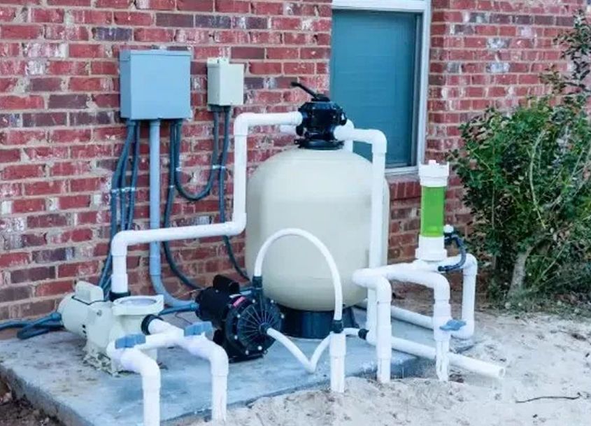 Outdoor pool filter system with pump and pipes next to a brick wall for efficient water circulation and cleaning.